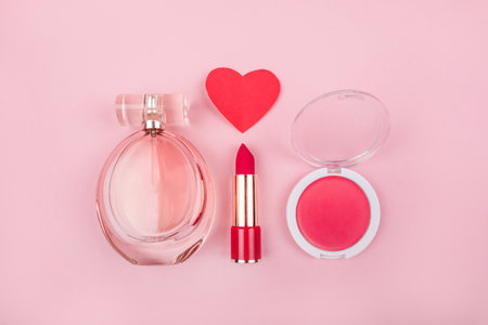 Valentines day flatlay with beauty products: bottle of perfumes, red lipstick, rose blush and paper heart on pink background.の写真素材