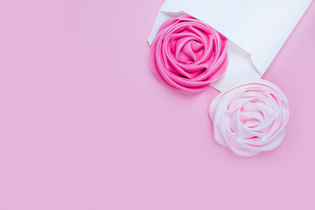 Beauty flatlay with colorful rose flower shaped meringue in white envelope on the pink background.の写真素材
