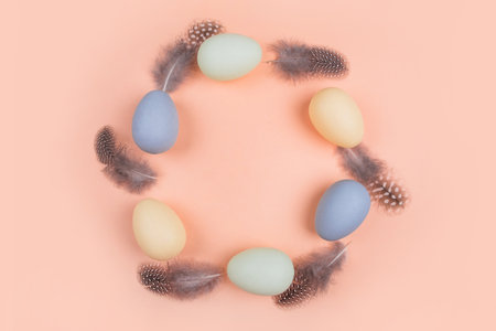 The circle of dyed on green, yellow and grey Easter eggs with feather isolated on peach background. Easter theme flatlay.の写真素材