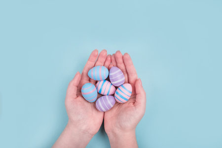 Woman hands holding dyed on blue, pink and violet Easter eggs in the straw basket isolated on blue background. Easter theme flatlay.の写真素材