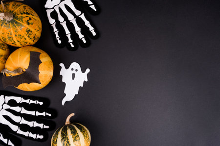 Top view of Halloween pumpkins, autumn leaves, paper craft bats, ghost, and skeleton on black background.の写真素材