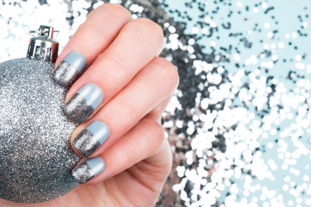 Woman hand with baubles and festive glitter manicure on blue shiny background. Christmas holiday concept.の写真素材