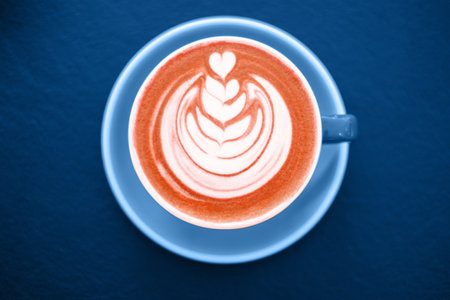 Cup of coral latte with beautiful latte art on the blue round table. Color of the year concept.の写真素材