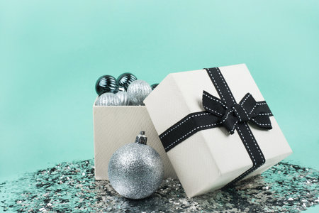 Biege gift box with silver and pine green christmas baubles inside on mint greeen background....