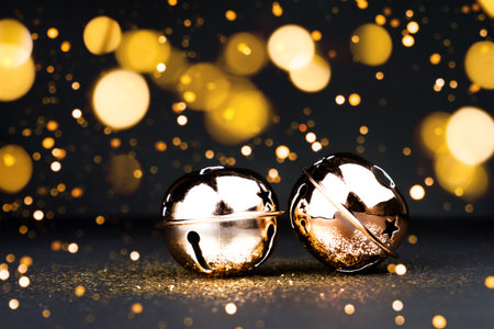 Two golden Christmas jingle bells on black background with glitter amd golden bokeh lightening. New Year concept.の写真素材