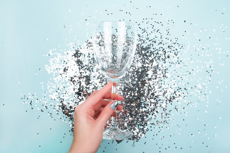 Woman's hands holding vine glass with festive glitter on blue shiny background. Christmas holiday concept.の写真素材