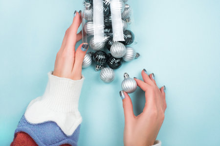 Woman's hands in sweater holding box with Christmas tree baubles isolated on blue background. Christmas holiday concept.の写真素材