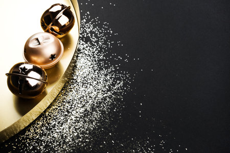 Three Christmas jingle bells and golden tray on black background with glitter. New Year concept.の写真素材
