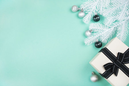 Christmas flatlay with beige gift box, silver baubles and white pine tree branches isolated on mint green background. New Year concept.の写真素材