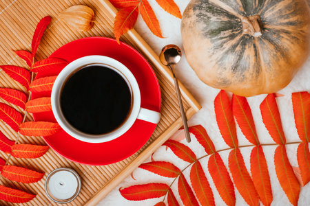 Autumn flatlay with cup of coffee with red plate on the wooden tray, gold spoon, candle, pumkin and red leaves.の写真素材