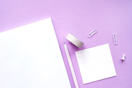 Beautiful office stationery flatlay with ruled notebook, pen, sticky note and paper clip on the bright desk with violet background.の写真素材