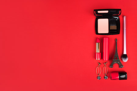 Valentines day flatlay with red lipstick, blush, makeup brush, nail polish, earrings and eiffel tower figurine isolated on red background.の写真素材