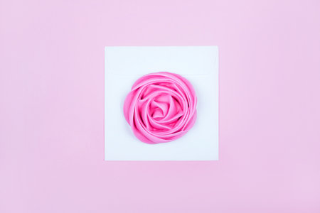 Beauty flatlay with colorful rose flower shaped meringue in white envelope isolated on the pink background.の写真素材
