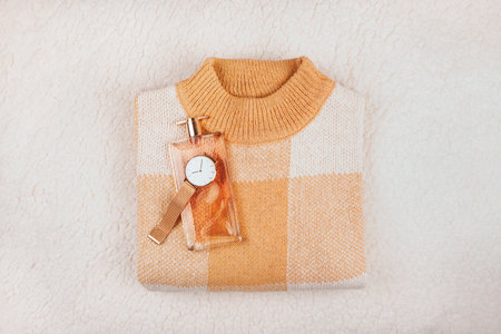 Fashion flatlay with beige sweater, perfume bottle and mesh strap watches on cozy off white blanket.の写真素材