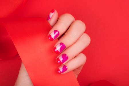Woman hand with bright manicure and shiny red ribbon isolated on red background.の写真素材