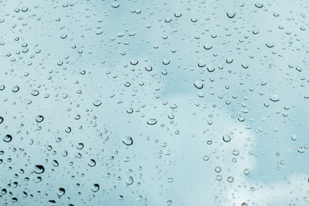 Rain drops on window pane glass surface with cloudy background.の写真素材