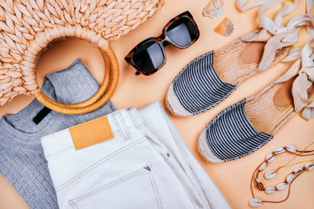 Summer fashion flatlay with white denim jeans, silver top, summer straw bag, striped espadrilles sandals, sea shell necklace and tortoiseshell sunglasses isolated on beige background.の写真素材