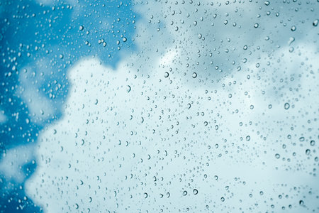 Rain drops on window pane glass surface with cloudy background.の写真素材