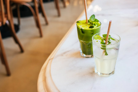 Two glasses of matcha green tea and classic lemonades with paper straw on marble table with blurred background.の写真素材