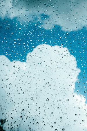 Rain drops on window pane glass surface with cloudy background.の写真素材
