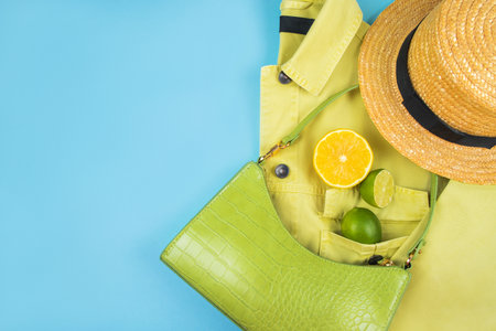 Bright summer citrus flatlay with lemons and limes in the green baguette bag, yellow denim jacket and straw boater hat isolated on yellow background.の写真素材