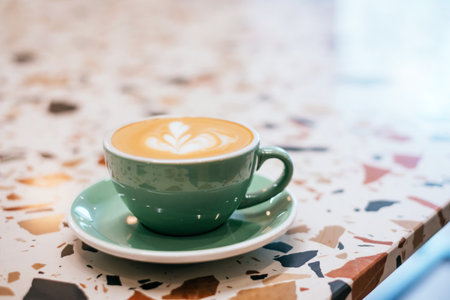 A cup of coffee with beautiful latte art in a green cup on a stone table background.