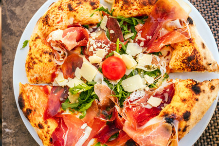Top view of plate with delicious Italian pizza with prosciutto, arugula, fresh tomatoes and shaved parmesan cheese.の写真素材