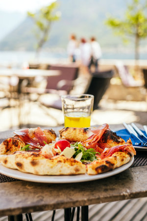 Top view of plate with delicious Italian pizza with prosciutto, arugula, fresh tomatoes and shaved...