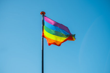 Rainbow flag waving in the wind against blue sky. Freedom and love concept. Pride month.の写真素材