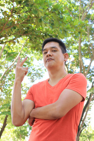 Asian man is showing two finger and natural backgroundの写真素材