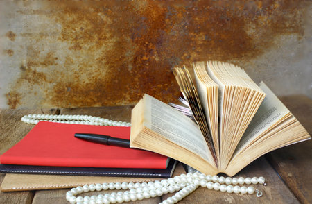 Old open book and red notebook on wooden tableの写真素材