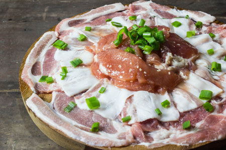 Pieces of raw pork with onion leafs on a wooden plateの写真素材