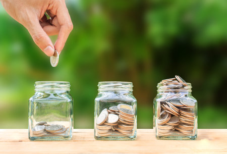 Conceptual hand putting coins into bottle on nature background,Business investment growth concept