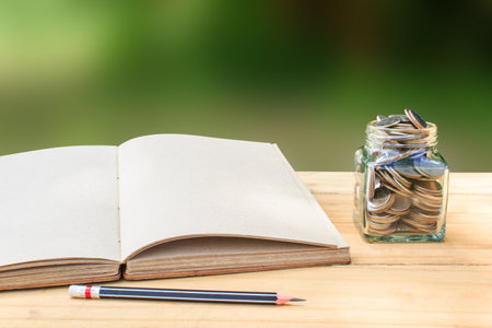 Book and Coin in glass jar on wooden table with pencil. Conceptual saving, invest, for education or futureの写真素材