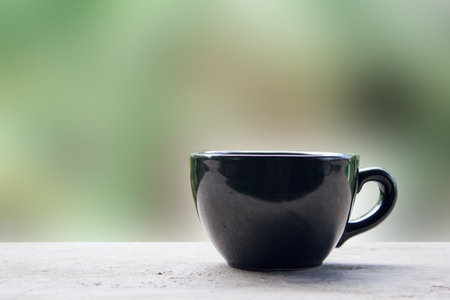 Black cup of coffee or tea on table with green abstract blurred background.の写真素材