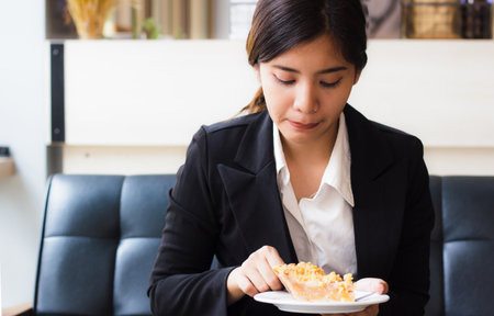 Asian business woman in relax time and eating apple pie in coffee shop. Hand holding  spoon used to eat pie. Apple pie, regional variation apple tart, which the principal filling ingredient is apple.の写真素材