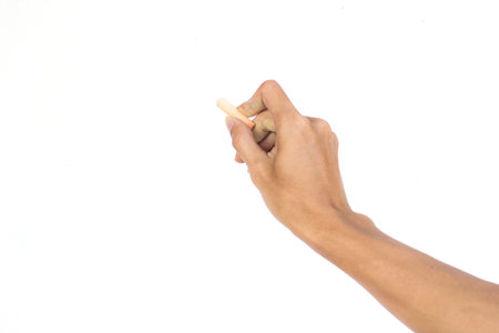 Hand holding chalk writing something text on empty space. Isolated on white background. Chalk is used to write text on a blackboard. Chalk made of plasterの写真素材