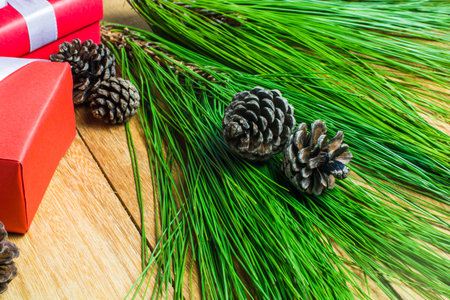 Pine cone and pine leaves background with red and white gift box on wood table. Christmas, New year,...
