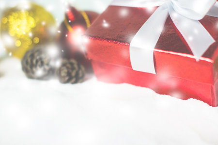 Close up red gift box white ribbon with Christmas ball and pine cones on snow with copy space....