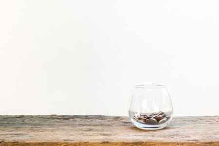 Many coins in clear glass on wooden table on white background with copy space.
