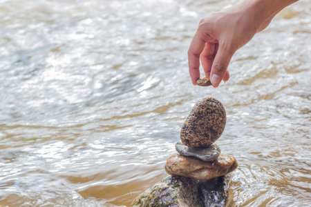 Hand putting stone on stacking stones  on the riverside. The stones are stacked on the river side. の写真素材