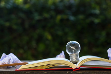 Light bulb growing on open book on the table in the public park with crumpled papers Idea nature...