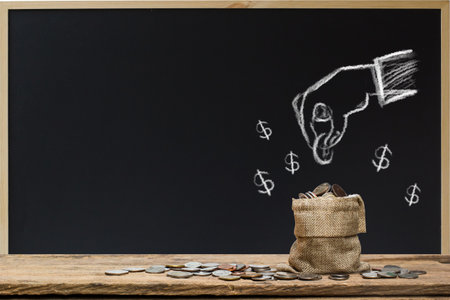 Saving money. Money investment concept. Hand drawing on chalkboard hand holding coin over money bag.の写真素材