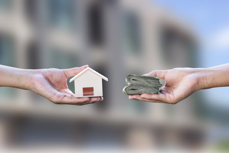 Home loan, mortgages, debt, home buying concept. Hand holding small resident exchange money on blurred real estate background. Exchange of finances and houses.の写真素材