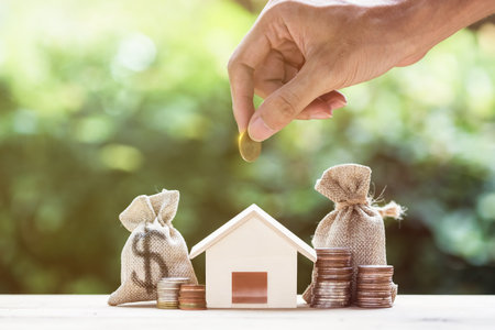 Saving money, home loan, mortgage, a property investment for future concept. A man hand putting money coin over small residence house and money bag with nature background. A sustainable investment.の写真素材