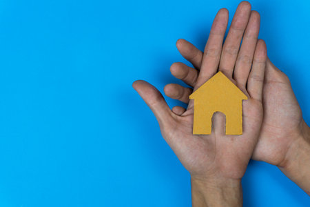 Buy or rent. A small house model made by paper cut on a man hand on  blue background.の写真素材