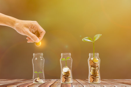 Saving and investment. Business and finance concept. Hand putting coins into glass jar with growing...