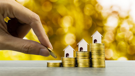 Property investment concept. Hand holding coin over a small house model on stack of coins. Depicts...