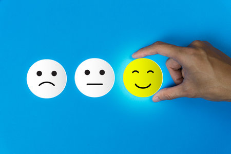 Conceptual the customer responded to the survey. The client using hand choose happy face smile icon on blue background. Depicts that customer is very satisfied. Service experience satisfaction concept.の写真素材