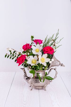 Fresh pink and Christmas roses in metal teapotの写真素材